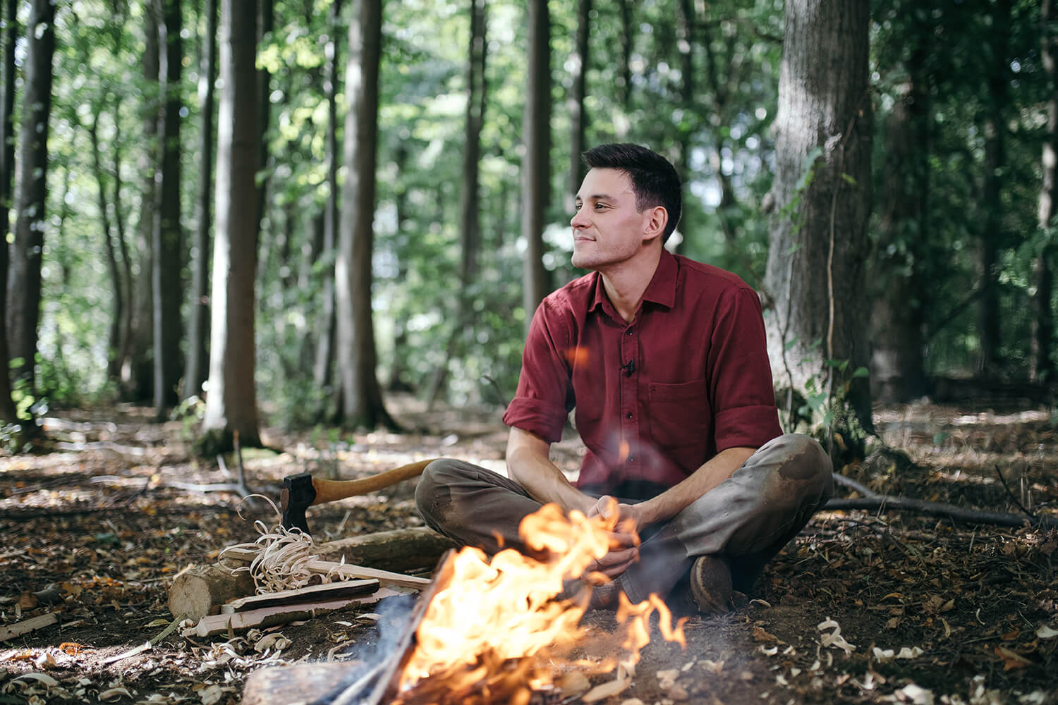 Dan Hume sits by a small fire in a forrest.